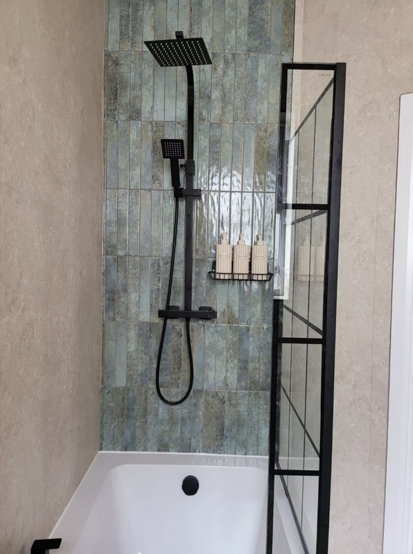 Modern bathroom shower area with black fixtures, tiled walls, and white bathtub