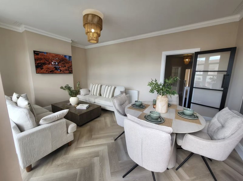 Modern living room with cream armchairs, round dining table, potted plants and gold ceiling light