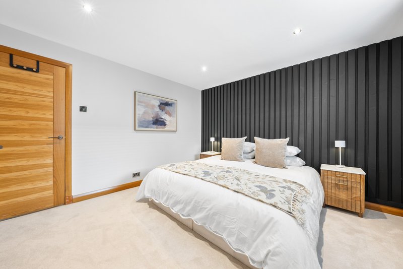 Modern bedroom with double bed, dark feature wall, wooden door and side tables