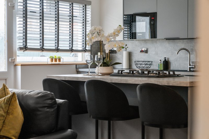 Modern kitchen with black bar stools, gas cooktop, and window with shutters