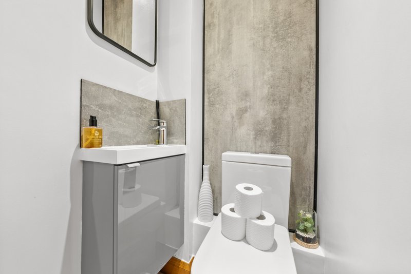 Modern bathroom with gray vanity, white sink, mirror, and toilet paper storage