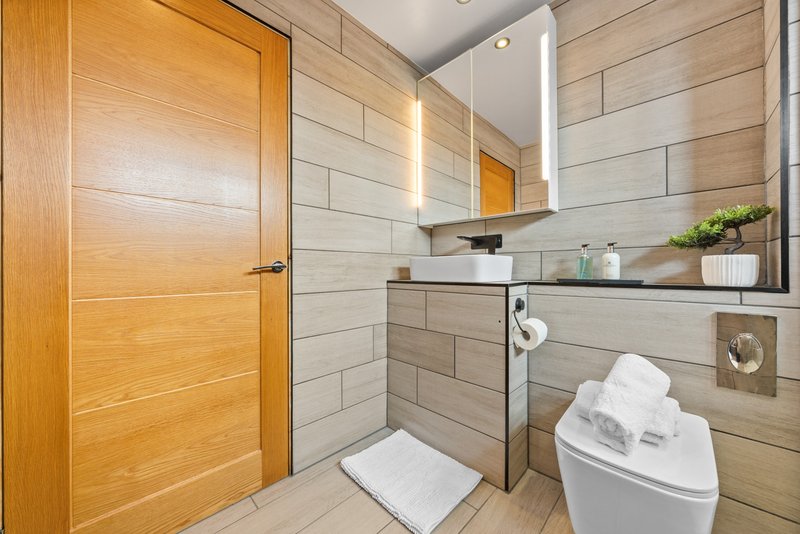 Modern bathroom with wooden door, beige tile walls, white sink and toilet, shelving