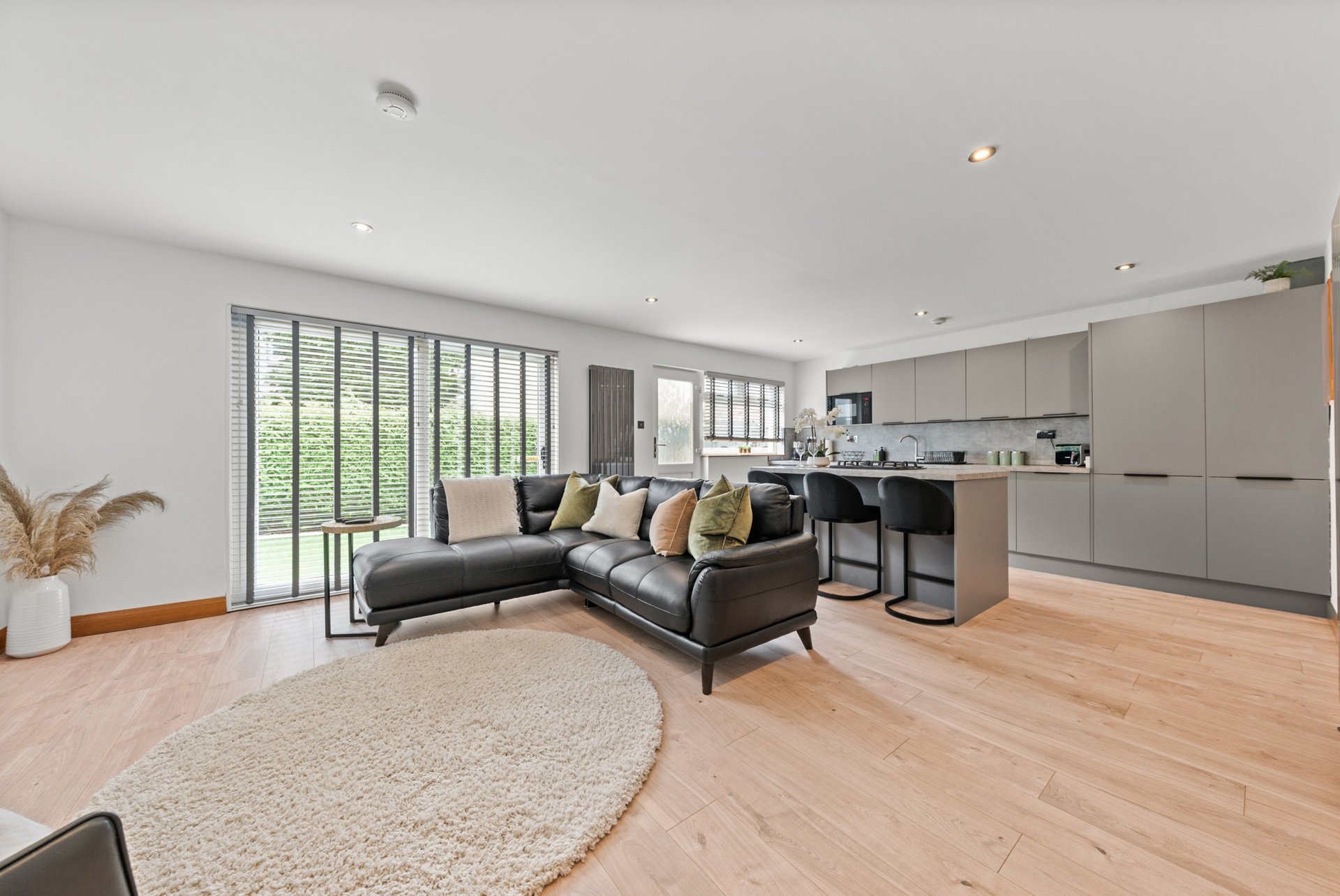 Open-plan living area with dark sofa, wooden flooring, kitchen, and garden doors