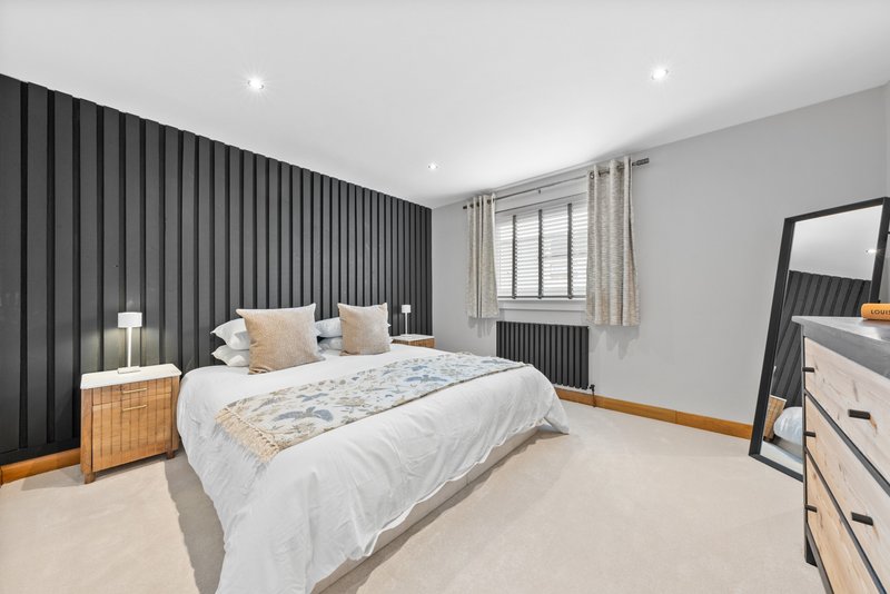 Modern bedroom with double bed, dark feature wall, wooden nightstands and floor mirror