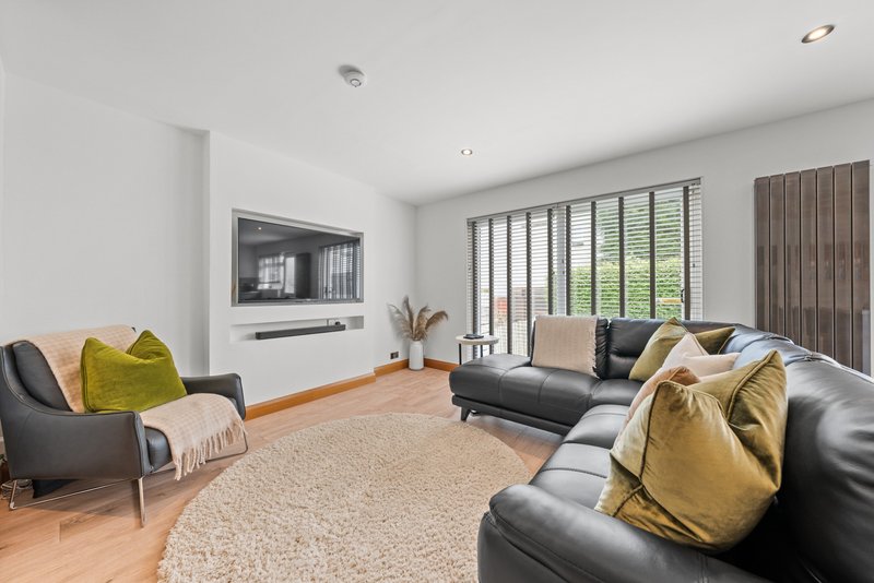 Modern living room with black leather sofa, armchair, wooden flooring, beige rug and wall-mounted TV