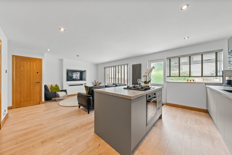 Open-plan kitchen and living area with gray island, white cabinetry, wooden flooring and seating area