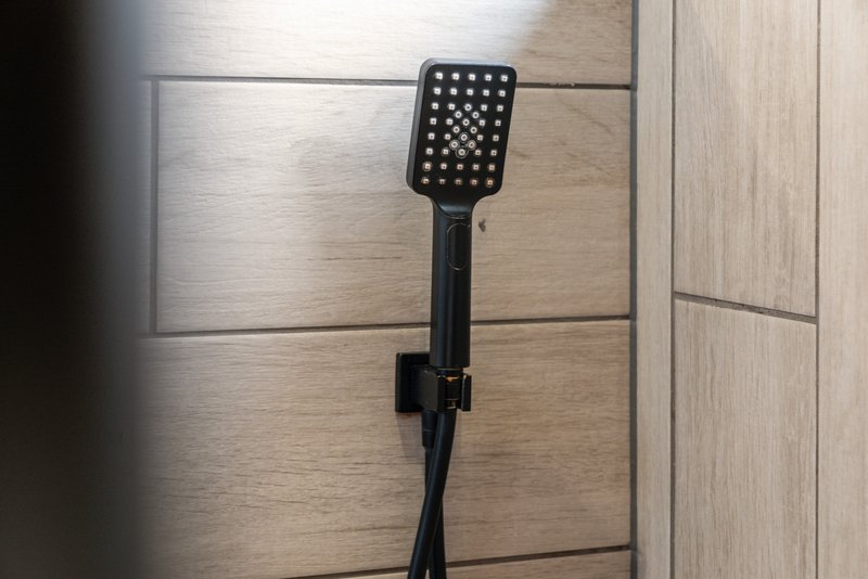 Black handheld shower head mounted on tiled bathroom wall with wood-grain surround