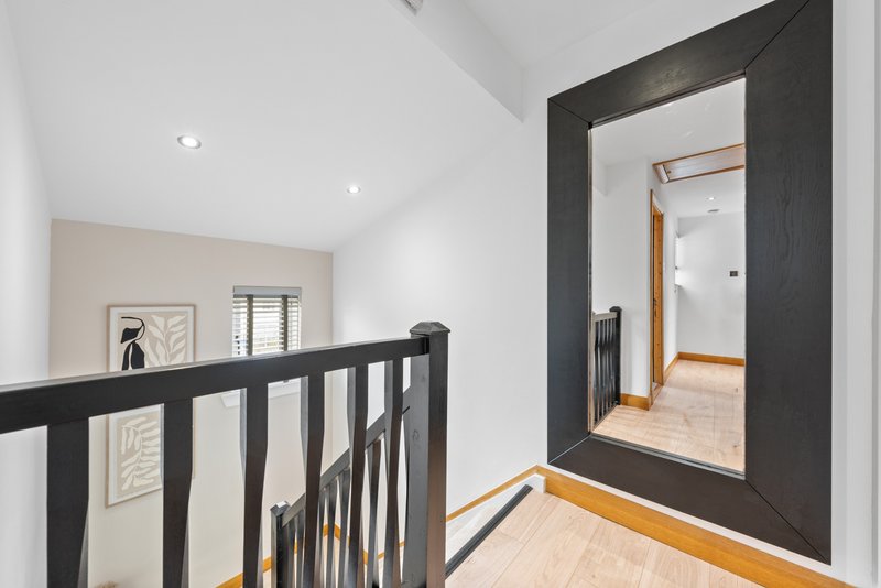 Modern hallway with black stair railing, wooden flooring, framed artwork and large mirror