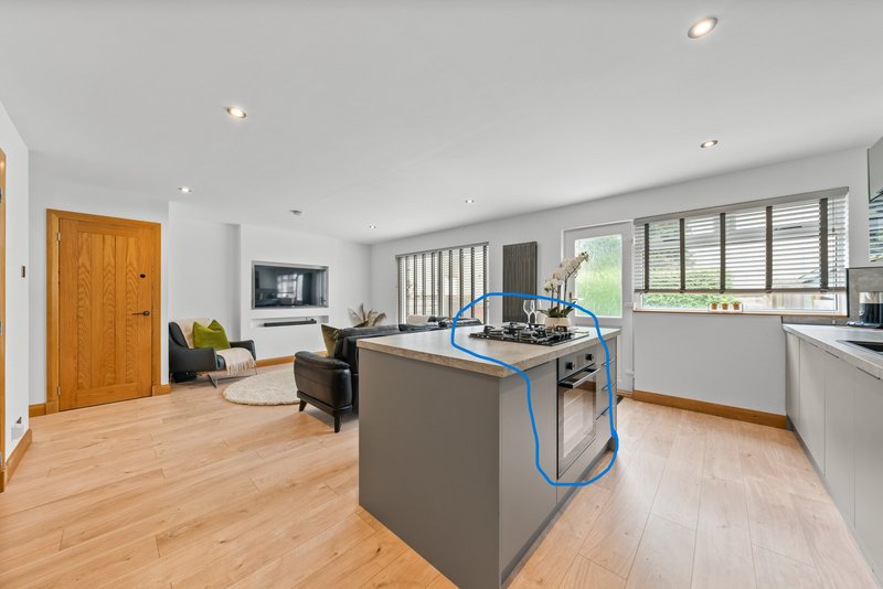 Open-plan kitchen and living area with wooden flooring, gray island, white cabinetry and lounge seating