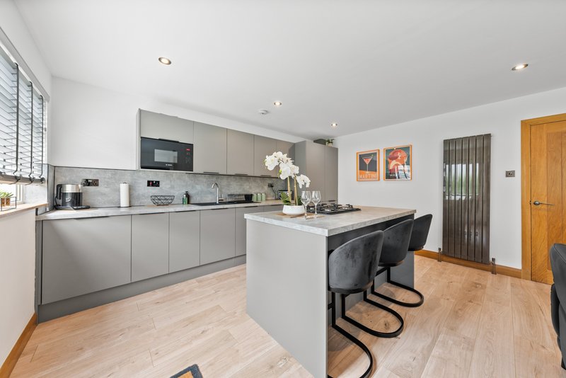 Modern kitchen with grey cabinetry, white island, wooden flooring and dining area