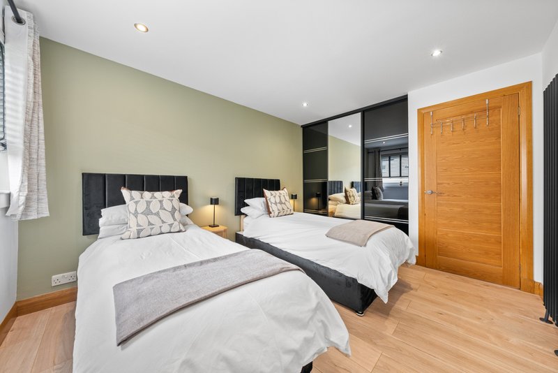 Modern bedroom with two single beds, mirrored wardrobe, wooden door and pale green walls