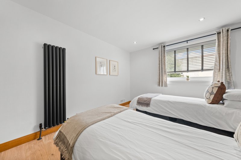 Bright bedroom with two beds, black radiator, wooden floor and window with shutters
