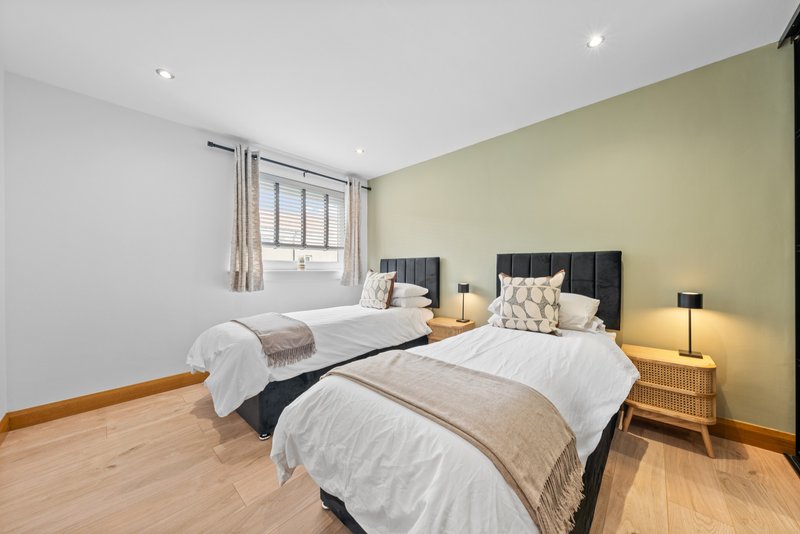 Bright bedroom with two single beds, yellow accent wall, wooden floor and bedside lamps