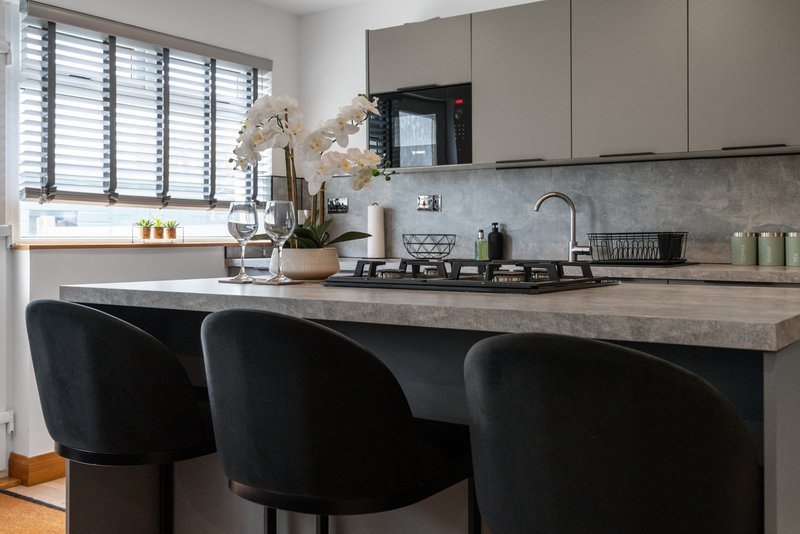 Modern kitchen with island seating, gas cooktop, grey cabinetry and window overlooking garden