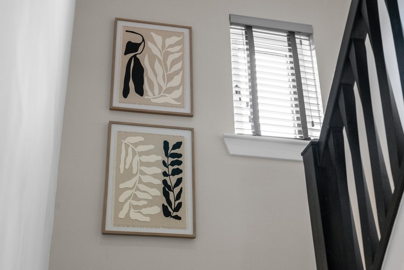 Bright stairwell with white walls, framed botanical prints, window with shutters, black stair rail