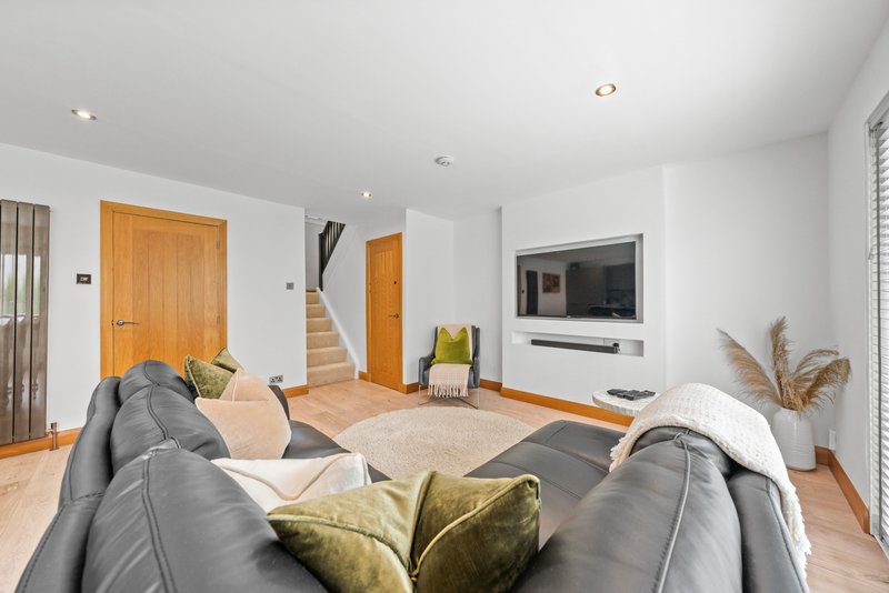 Open-plan living room with grey sofa, wooden doors, TV, and staircase access
