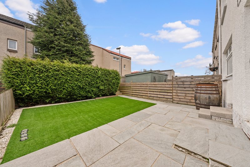 Spacious backyard garden with paved patio, manicured lawn and wooden fence