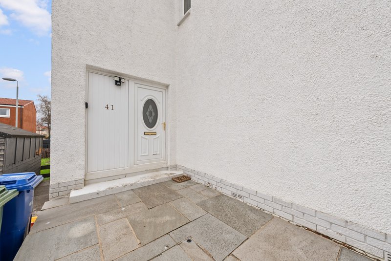 White-rendered house exterior with entrance door, paved patio, and side wall