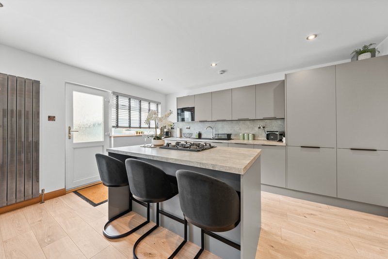 Modern kitchen with island, gas hob, black bar stools and light wooden flooring