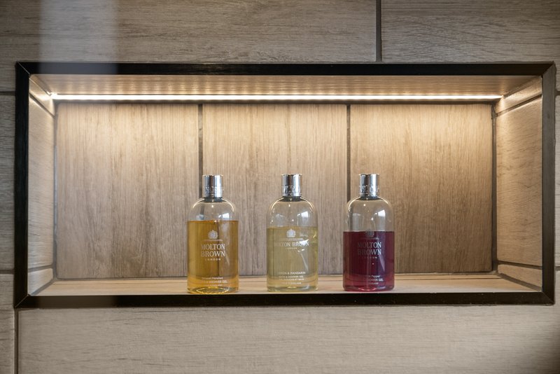 Wall-mounted wooden shelf displaying three glass bottles with amber and burgundy liquids