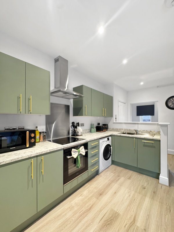 Modern kitchen with sage-green cabinets, stainless steel appliances, and light wood flooring