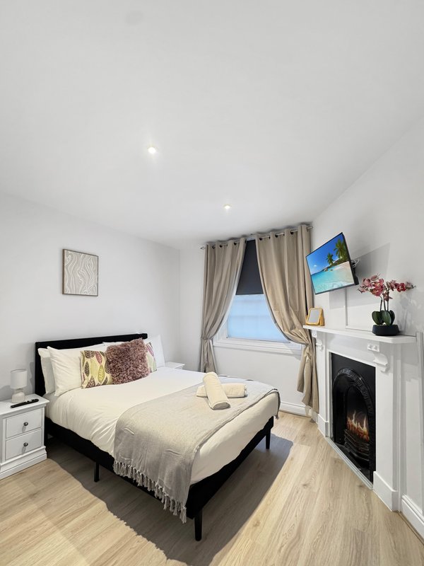 Bright bedroom with double bed, fireplace, TV, window with curtains and wooden floor