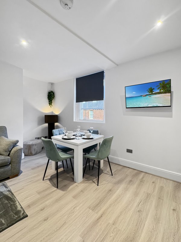 Modern dining area with white table, green chairs, and wall-mounted TV in bright apartment