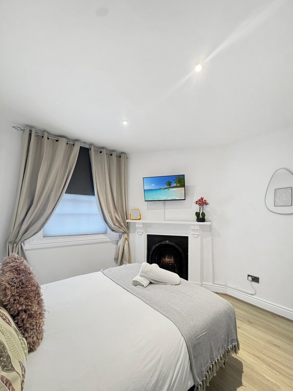 Bright bedroom with double bed, fireplace, wall-mounted TV, window with beige curtains