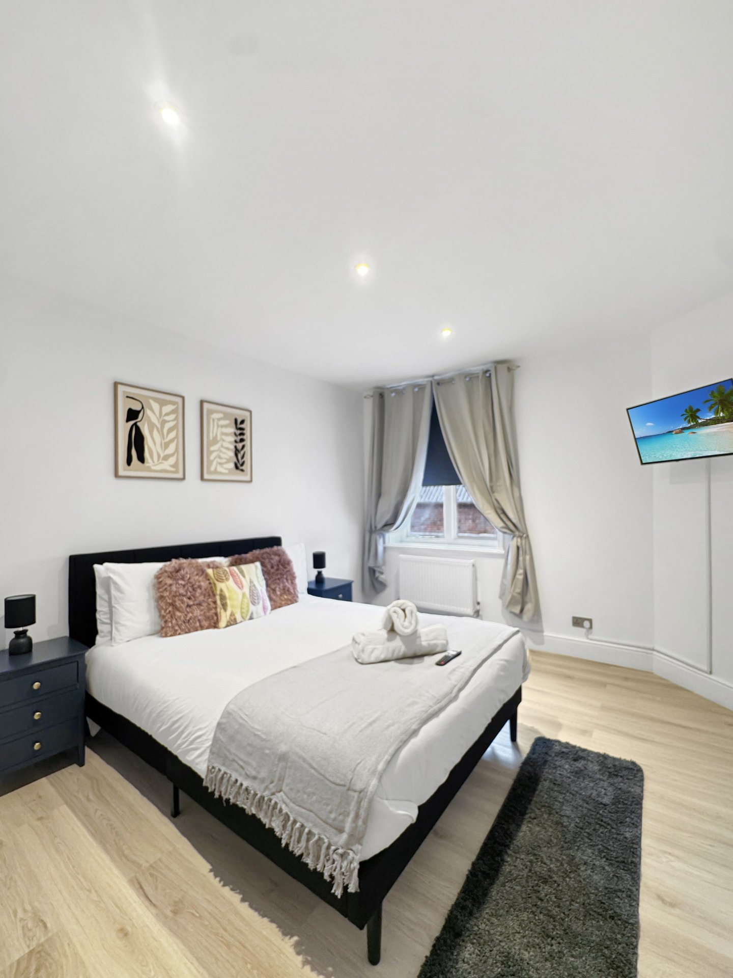 Bright modern bedroom with double bed, black frame, wooden floor and window with grey curtains