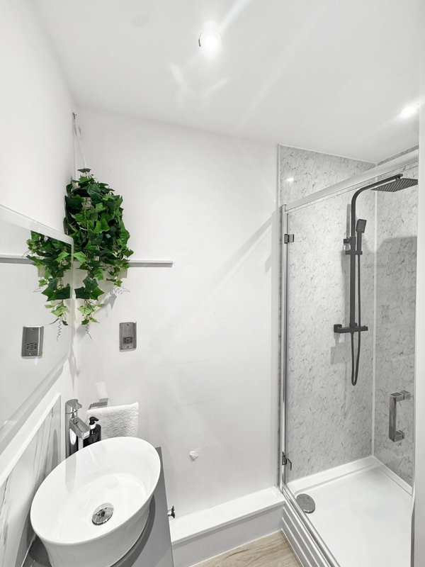 Modern bathroom with white oval sink, wall-mounted plant, and walk-in shower enclosure