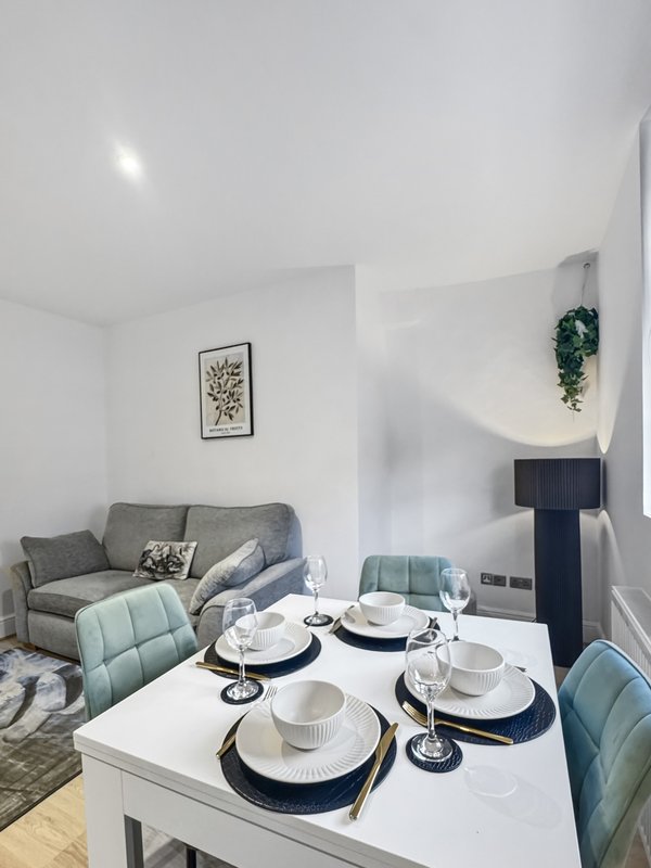 Modern open-plan living and dining area with grey sofa, set dining table and kitchen visible