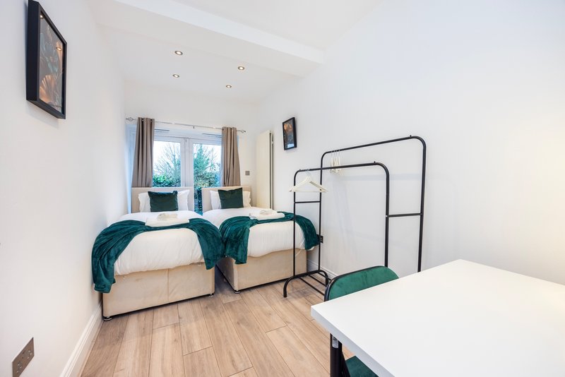 Bright bedroom with two single beds, metal frame, teal throws, wooden floor and windows