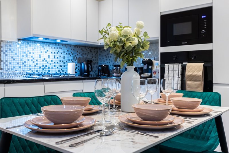 Modern kitchen with blue mosaic backsplash, white cabinetry, dining table set with place settings and flowers