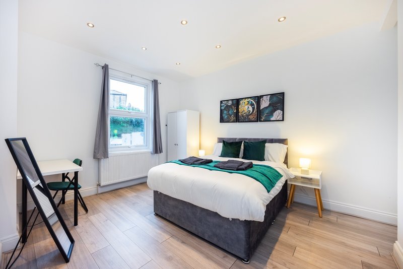 Bright modern bedroom with double bed, green bedding, wooden floor and window