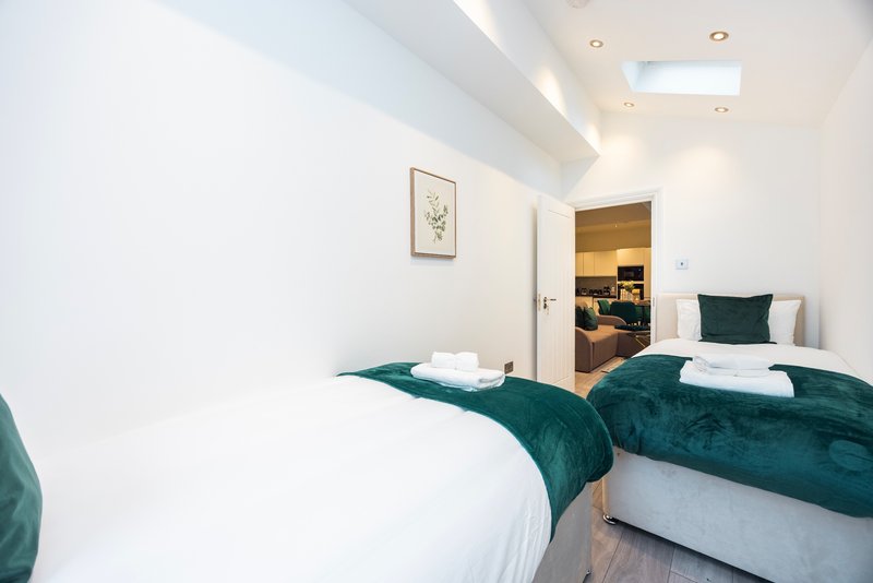 Modern bedroom with two single beds, teal bedding, white pillows, and skylight ceiling