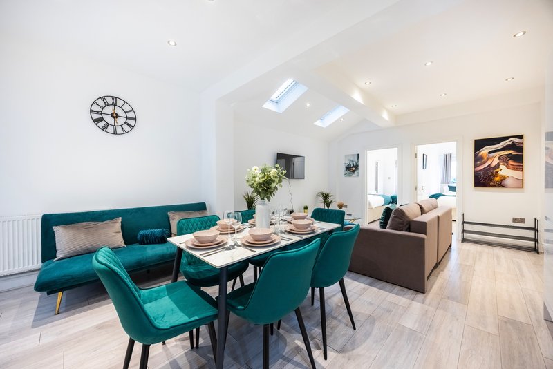 Open-plan living and dining area with teal seating, dining table, and skylight ceiling
