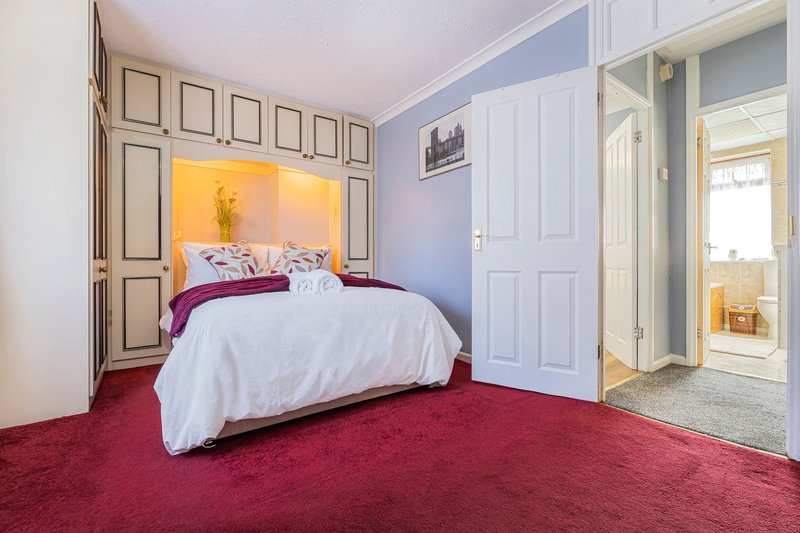 Bedroom with double bed, white bedding, burgundy carpet, and framed wall art