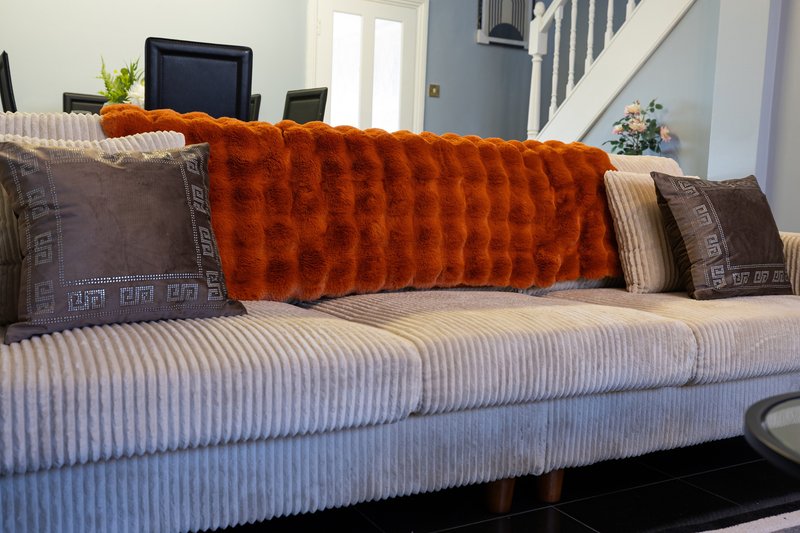 Living room sofa with orange throw blanket, patterned cushions and striped upholstery