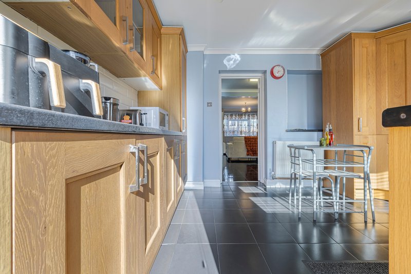 Modern kitchen with wooden cabinets, open shelving, and dark tile flooring extending to dining area