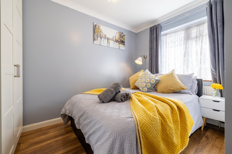 Modern bedroom with double bed, yellow throw, gray pillows and natural light from window