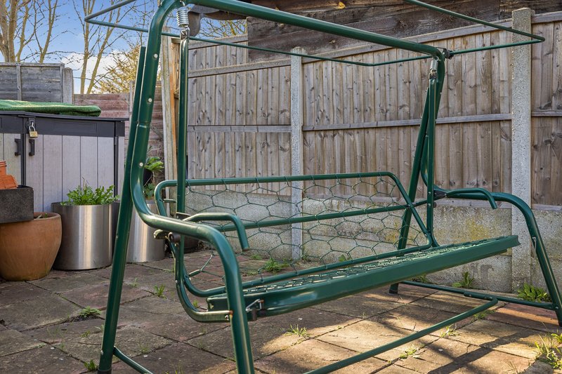 Garden patio with green metal swing seat, wooden fence, potted plants and paving