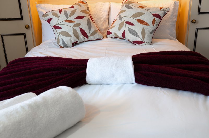 Bedroom with double bed, decorative pillows, burgundy throw blanket and rolled towels