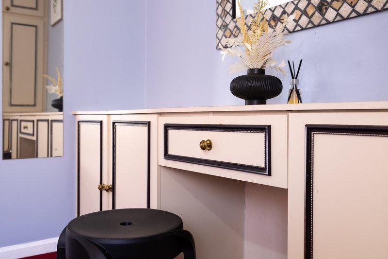 Modern bedroom vanity with white drawers, black round stool, decorative vase and dried flowers