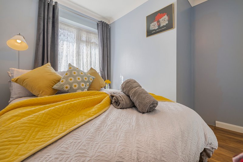 Bedroom with double bed, yellow bedding, decorative pillows, grey curtains and pendant lamp