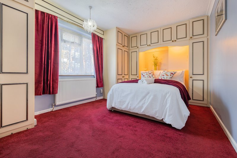 Spacious bedroom with double bed, red carpet, burgundy curtains and pendant light fixture