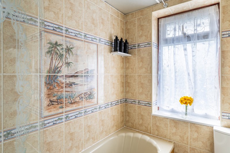 Bathroom with tiled walls, decorative tile mural, bathtub and window with yellow flowers