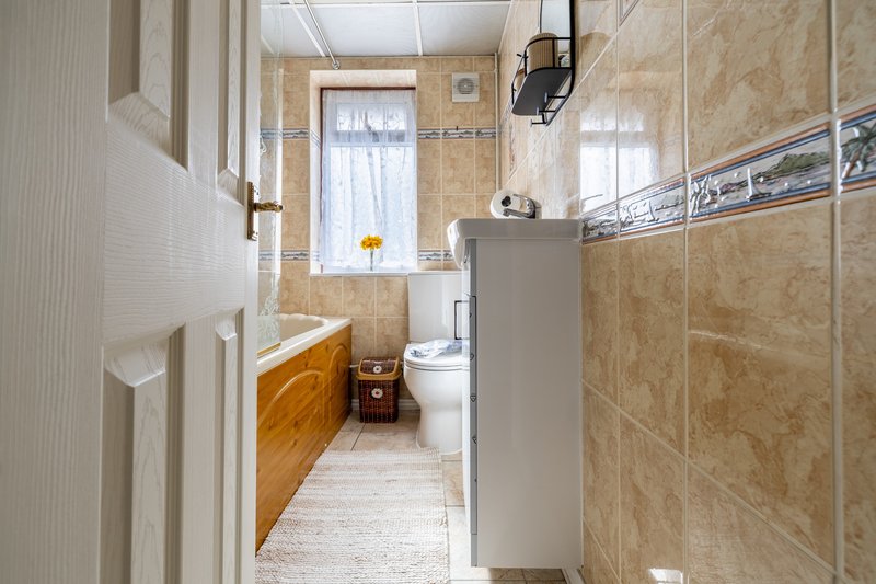 Bathroom with wooden vanity, toilet, tiled walls, window and wall-mounted fixtures