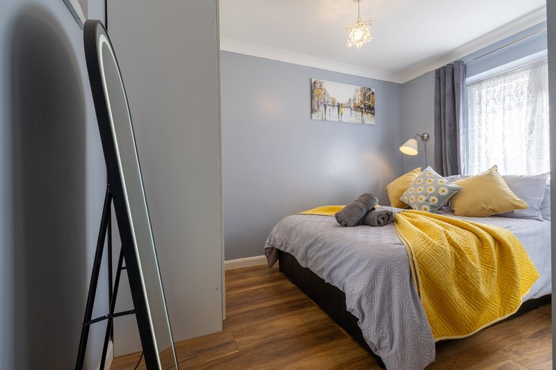 Bright bedroom with double bed, yellow bedding, wooden floor and pendant light