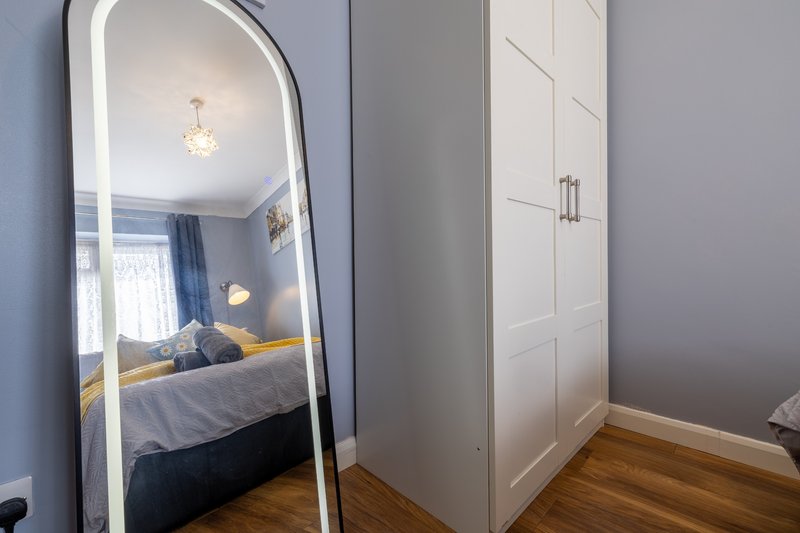 Modern bedroom with large floor mirror, white wardrobe, wooden floor and pendant light