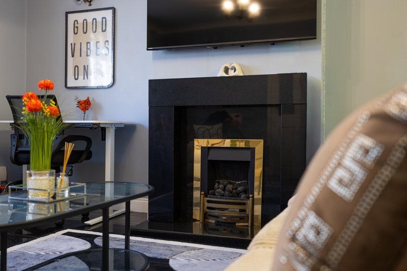 Modern living room with fireplace, TV, flowers in vase, and decorative wall sign